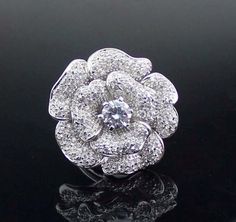 a white gold and diamond flower ring on a black surface with reflective reflection in the foreground