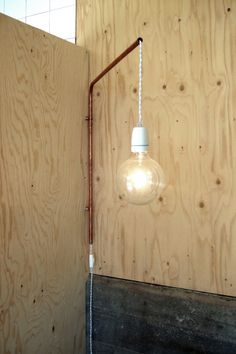 a light bulb hanging from the side of a wooden wall next to a metal pipe