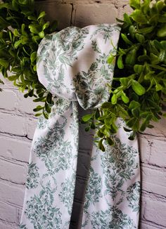 a green and white scarf hanging on a brick wall next to a bush with leaves