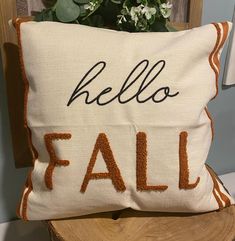 a pillow with the words hello fall on it sitting on a wooden chair next to a potted plant