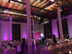 an indoor event venue with purple lighting and white linens on the tables, along with tall columns