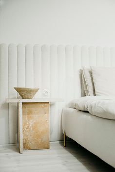 a white bed sitting in a bedroom next to a table with a vase on it