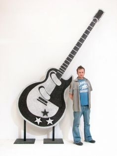 a man standing in front of a guitar sculpture with his hand on the back of it