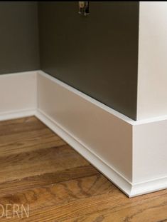 the corner of a room with wood flooring and white trim on the bottom part of the wall