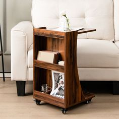 a small wooden table on wheels with a magazine rack underneath it and a white couch in the background