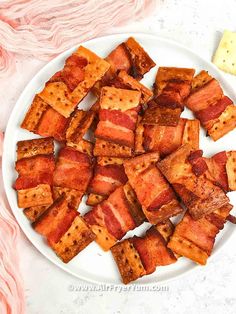 bacon cubes on a white plate next to some crackers and a pink blanket