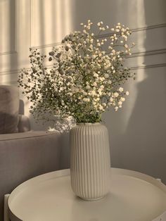 a vase filled with white flowers sitting on top of a table next to a couch