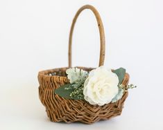 a white flower in a wicker basket with green leaves and flowers on the handle