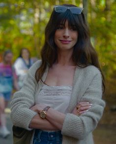 a woman with her arms crossed standing in front of some people wearing sunglasses and sweaters