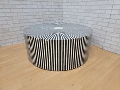 a black and white striped stool sitting on top of a hard wood floor next to a brick wall