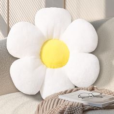 a flower shaped pillow sitting on top of a couch next to a pair of glasses