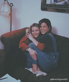 two women sitting on top of a couch hugging each other and smiling at the camera