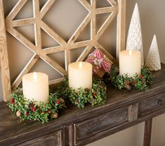 candles are sitting on a mantle decorated with greenery and pine cones