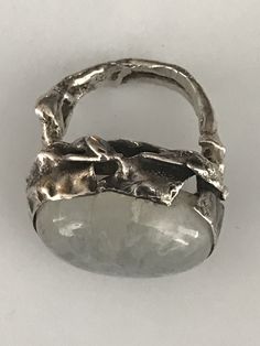 "This unusual ring has a large oval shaped cabochon moonstone that is bezel set in south-west fashion. The band looks almost like branchlike wavy lines. The silver setting which is raised to hug the stone has a hammered and pinched look and has some areas where it looks like the silver has split which is part of the design. The face of this ring is 3/4\" long and about 1\" at its widest. It shows as a size 4 1/4 on my ring sizer, but fits my size 5 finger. Please see all photos for details, as w Handmade Oval Moonstone Ring In Modern Style, Modern Handmade Oval Moonstone Ring, Modern Oval Moonstone Ring With Large Stone, Handmade Modern Oval Moonstone Ring, Hand Forged Oval Moonstone Ring, Unique Silver Oval Cabochon Moonstone Ring, Unique Silver Moonstone Ring Oval Cabochon, Unique Silver Moonstone Ring With Oval Cabochon, Unique Moonstone Ring With Large Stone