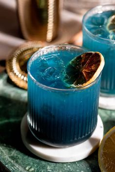 two glasses filled with blue liquid and garnished with an orange slice on the rim