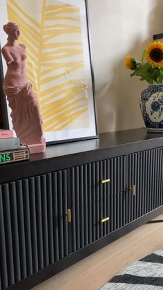 a vase with sunflowers is sitting on a black cabinet in the living room