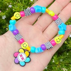 a child's hand holding a colorful bracelet with smiley face charms on it and flowers in the background