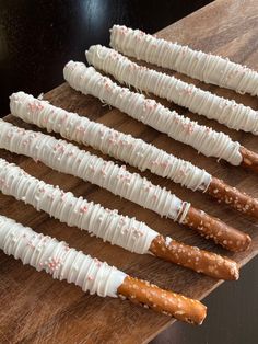 six pretzels are lined up on a wooden board with white icing and sprinkles