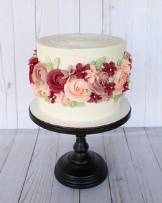 a white cake with pink and red flowers on it sitting on top of a wooden table