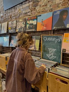 a woman looking at records on display in a music store with brick walls and posters behind her