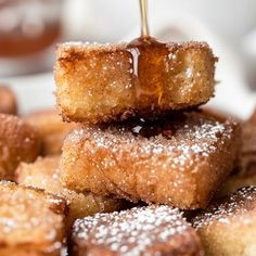 some sugared doughnuts stacked on top of each other and being drizzled with syrup