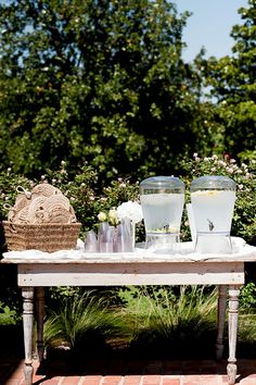 an old table with two ice buckets and glasses on it in front of some bushes