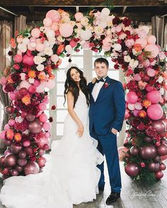 a man and woman standing in front of a decorated arch with balloons on it's sides