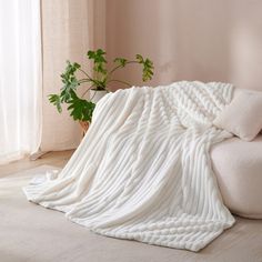 a large white blanket sitting on top of a couch next to a potted plant