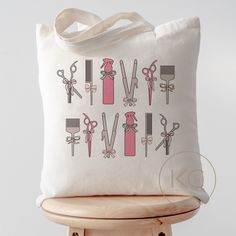 a white tote bag with scissors and hairbrushes on it sitting on top of a wooden chair