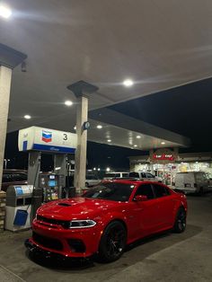 a red car is parked in front of a gas station with other cars at night