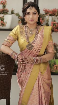 a woman in a yellow and pink sari with jewelry on her neck, standing next to a chair