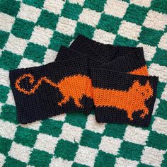 two black and orange knitted animal mittens on a green and white checkered blanket