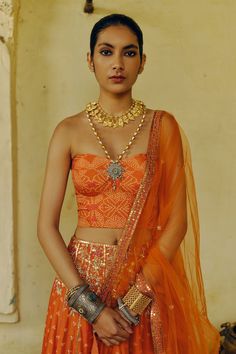 Rust orange attached cancan flared lehenga with all over bandhej phool print and cascading bloom embroidery using aari, sequins, gota, dori, anchor and zardozi highlights. Paired with an off shoulder corset style bandhani printed padded blouse and an aari-sequin vine border embroidered net dupatta. - Aza Fashions Orange Dupatta For Reception And Festivals, Orange Sets For Reception And Festivals, Orange Choli With Dupatta For Reception, Orange Lehenga For Festivals And Reception, Orange Lehenga For Reception And Festivals, Orange Traditional Wear For Diwali Reception, Orange Traditional Wear For Reception And Diwali, Traditional Orange Sets For Reception, Orange Zari Work Sets For Wedding