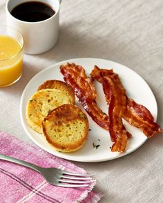 bacon and biscuits on a white plate next to a glass of orange juice