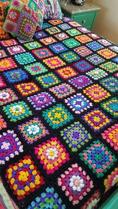 a crocheted granny blanket on top of a bed with colorful pillows and blankets