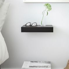 there is a vase with flowers and glasses on the shelf above the bed, next to a pair of reading glasses