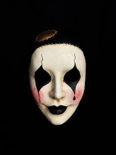 a white mask with black and red paint on it's face, against a black background