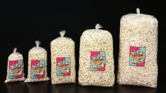 five bags of popcorn sitting next to each other on a black surface with one bag filled with rice