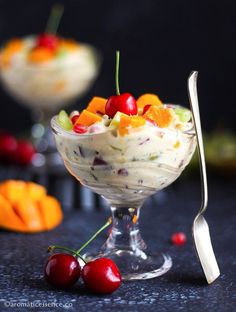 fruit salad in a glass bowl with two spoons and cherries on the side