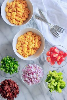 four bowls filled with different types of food on top of a marble counter next to utensils