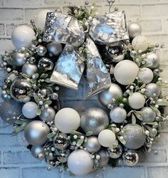 a wreath with silver and white ornaments hanging on a brick wall in front of a door