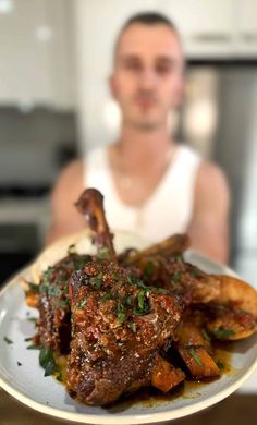 a man holding a plate with some meat and potatoes on it in front of him