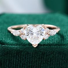 a heart shaped diamond ring sitting on top of a green cloth