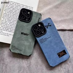 two iphone cases sitting next to each other on top of a bed with an open book