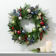 a christmas wreath and two candles on a mantle