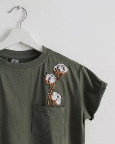 a t - shirt with three cotton flowers in the pocket on a white hanger