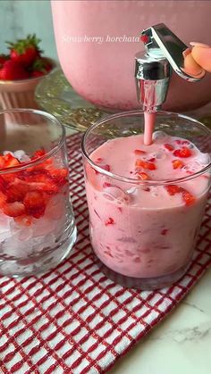 someone is pouring strawberries into a dessert in a glass bowl on a red and white checkered tablecloth