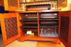 an open cabinet with wine glasses in it and lights on the top shelf, along with other items