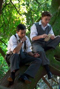 two young men sitting on a tree reading books