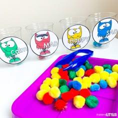 the plastic tray is filled with pom poms and some cups are next to it